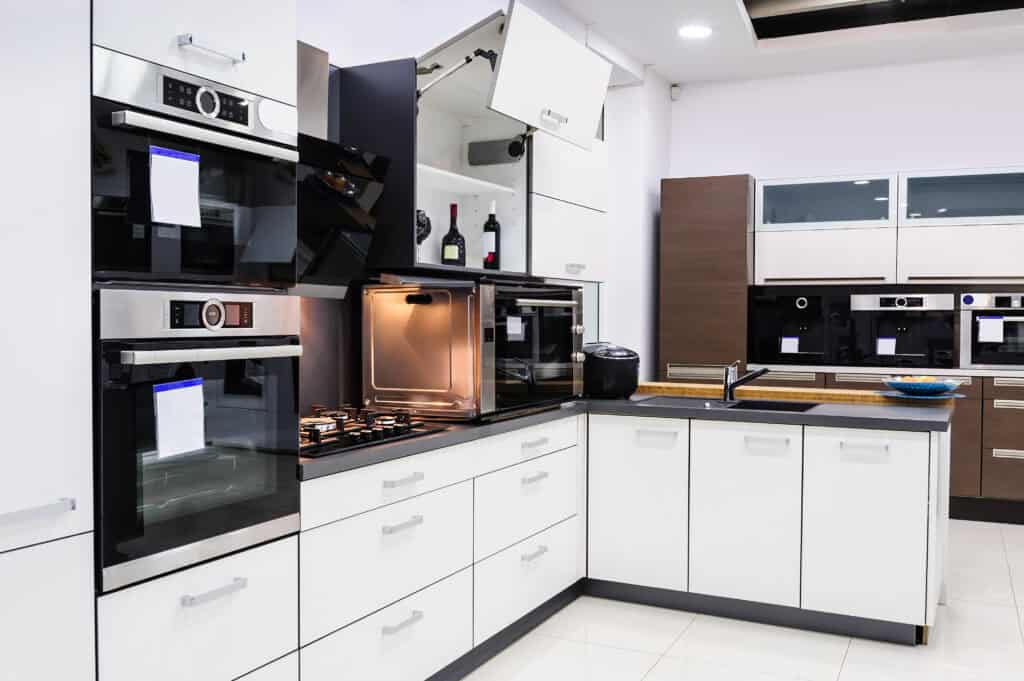 A modern kitchen featuring sleek white cabinets, built-in double ovens from top home appliance brands, and open cabinet doors. The elegant design includes a black countertop, a stovetop with burners, and a stylish display of wine bottles.
