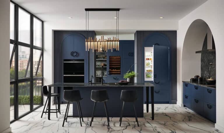 Modern kitchen with navy cabinets, black island and stools, pendant light, marble floors, built-in appliances, and large windows with a city view.