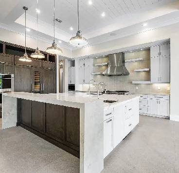 Modern kitchen with a large island, pendant lighting, stainless steel appliances, white cabinets, and a wood accent on the island base.