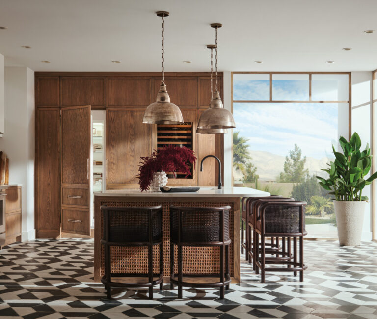 Modern kitchen with wood cabinets, a central island with four woven stools, pendant lighting, geometric tile flooring, and large windows letting in natural light.