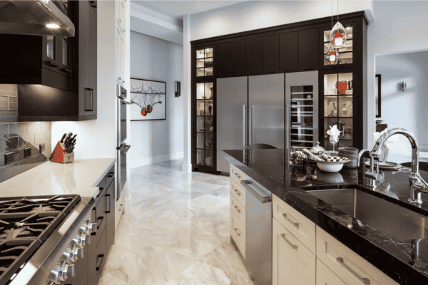 Modern kitchen with stainless steel appliances, marble floors, black and white cabinetry, a large island with a sink, and pendant lighting.